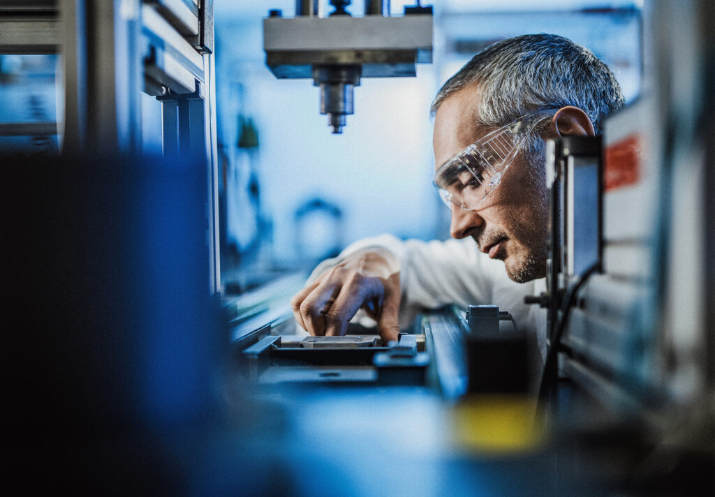 A man in safety glasses looks at an object in front of him.