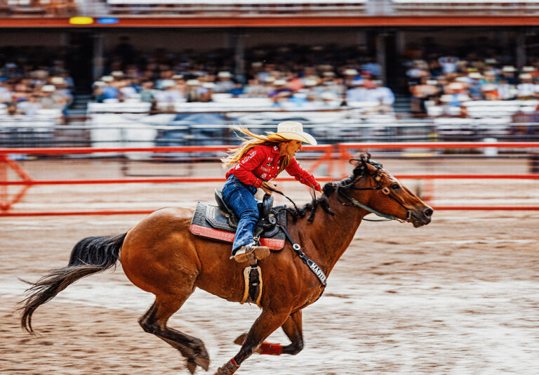 A woman rides a horse through a rodeo arena
