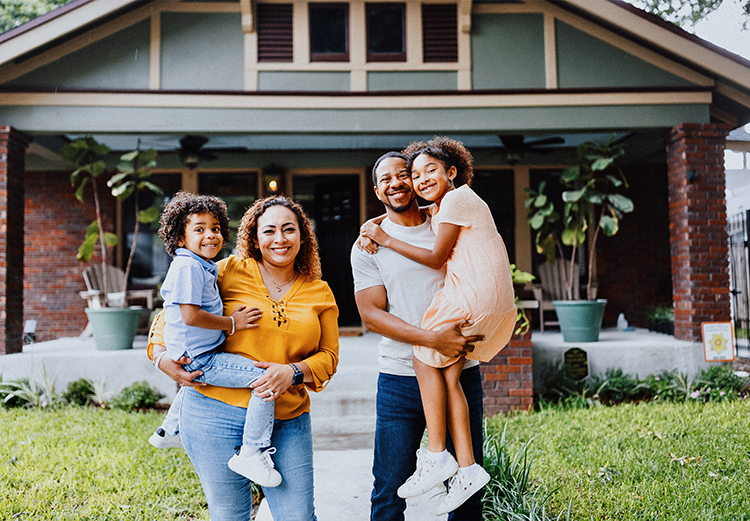 A man and woman pose with two small girls in front of a house.