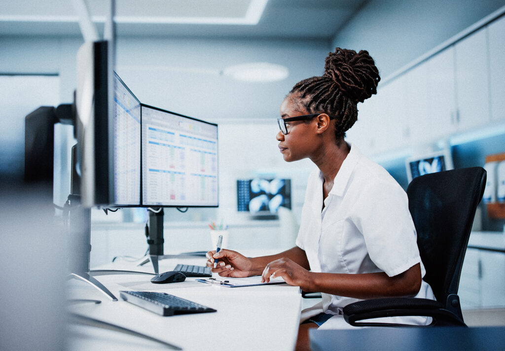 A woman in scrubs reviews information on a computer screen.