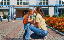 A woman kisses a small girl on the head in front of a school