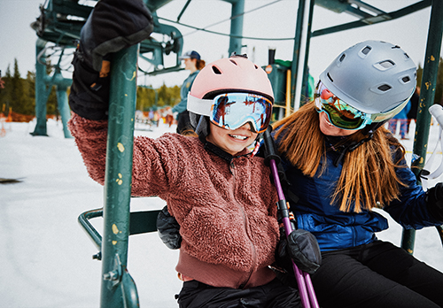 A woman and young girl sit together on a ski lift chair.