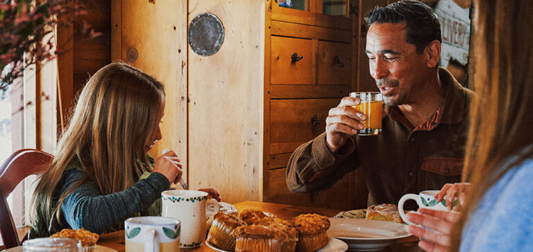 A man, woman, and a child enjoy breakfast at a wooden table.