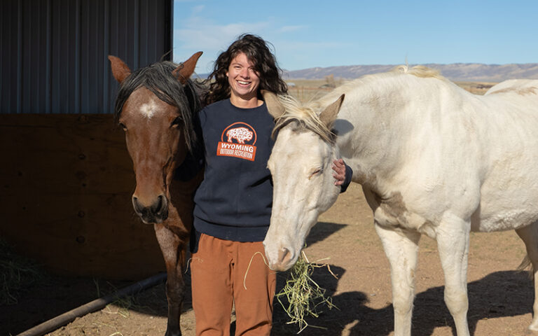 A woman stands, smiling, between two horses.