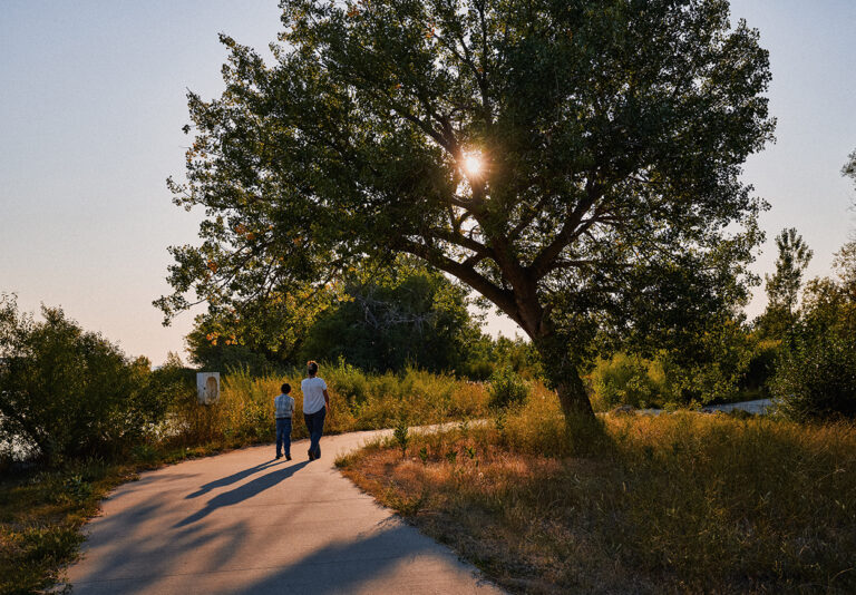 A woman and boy walk down a path, surrounded by trees.