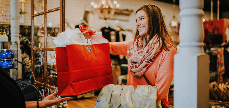 A smiling women holds a bag of purchases at a retail store.