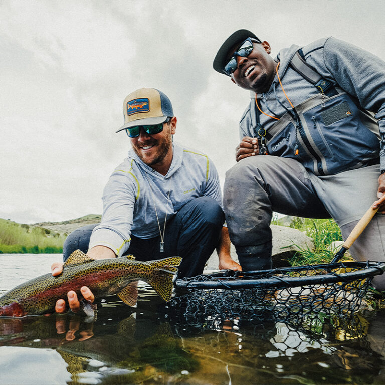 Two men pose in the water with a fish and fishing net.