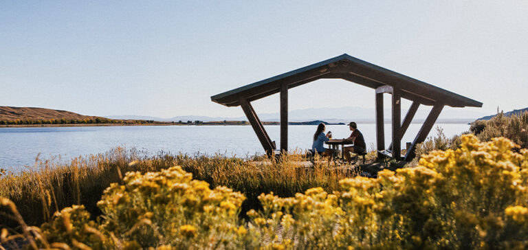 A male and female sit at a picnic table next to a lake.