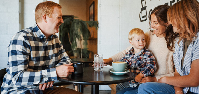 A smiling family gathers around a table with drinks.